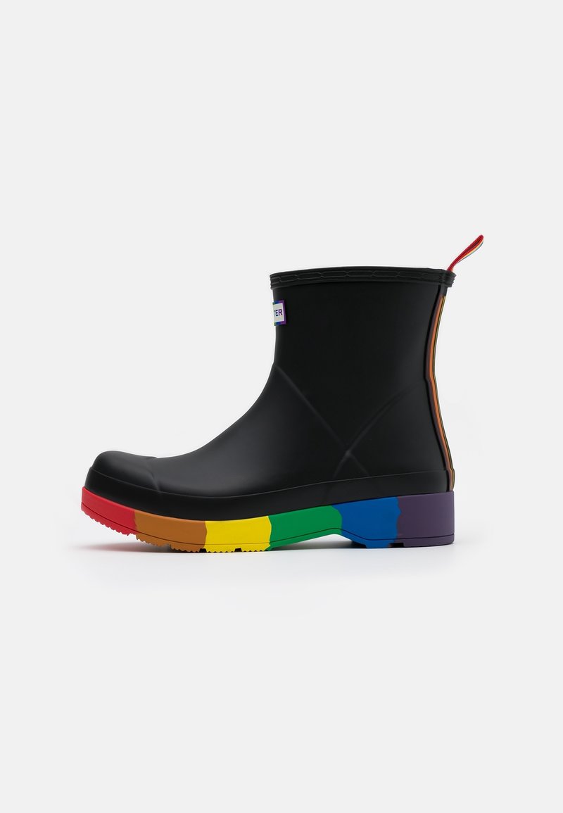 Botte cheville en caoutchouc noir avec une semelle à rayures multicolores. Dotée d'une languette de tirage rouge et d'une petite étiquette logo sur le côté. Texture lisse sur toute la surface.