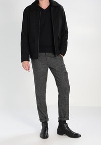 Veste noire zippée avec col en fourrure contrastante, associée à un pantalon gris texturé et des bottines noires. Coupe décontractée et design moderne.