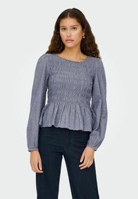 Blaue Peplum-Bluse mit langen Ärmeln und gerafftem Oberteil. Leicht strukturierter Stoff mit kleinen Akzenten, runder Ausschnitt und Volantsaum.