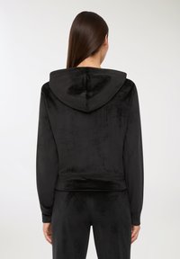 Felpa nera con cappuccio in morbido materiale vellutato. Presenta una vestibilità rilassata, maniche lunghe e un orlo corto. Texture liscia, design minimale.