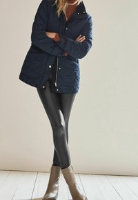 Giacca trapuntata blu navy, maglione marrone, leggings neri e stivali alla caviglia grigi. Texture morbide e silhouette aderenti creano un look a strati.
