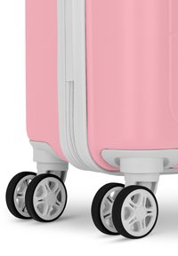 Roze harde koffer met een gestructureerd oppervlak, witte rits en vier multidirectionele wielen met zwarte rubberen profiel.