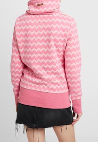 Hoodie rosa con motivo zigzag bianco, realizzato in tessuto morbido. Presenta un collo alto e polsini a coste, abbinato a una gonna di denim nera.