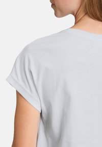 T-shirt blanc en coton avec des manches courtes retroussées, une coupe décontractée et une texture douce. Vue arrière montrant un subtil détail de couture au niveau du cou.
