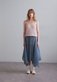 Pinker, ärmelloser Top mit Pailletten und V-Ausschnitt, kombiniert mit einem fließenden, asymmetrischen blauen Plisseerock und weißen Sneakers. Glatte Textur, leichtes Design.