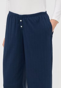 Tmavě modré žebrované pohodlné kalhoty s elastickým pasem, které mají dva malé knoflíky ve tvaru srdce a boční kapsy.
