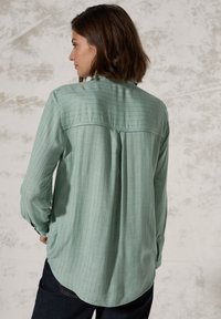Camicia a maniche lunghe verde chiaro con yoke posteriore e dettagli con pieghe, caratterizzata da sottili strisce verticali e una texture liscia.