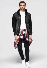 Giacca di jeans nera con cappuccio, t-shirt bianca, jeans neri e sneaker bianche. Camicia a quadri rossa e nera legata in vita.