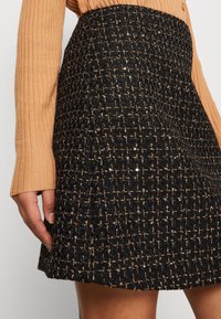 Falda negra con hilos dorados, que presenta un patrón tejido texturizado. Incluye sutiles lentejuelas, un diseño acampanado y un acabado suave en el dobladillo.