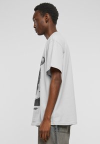 Light grey oversized t-shirt with short sleeves, featuring a graphic print on the front, made of soft cotton fabric.