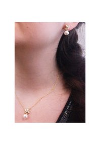 Gouden ketting en bijpassende oorbellen met een pareldruppel. De ketting heeft een delicate schakel en de oorbellen bevatten een decoratieve acccent.