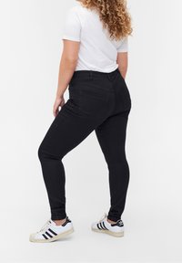 Jeans skinny negros con una cintura alta y dos bolsillos traseros, combinados con una camiseta blanca de manga corta y zapatillas blancas con detalles en negro.