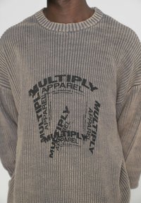 Grauer gerippter Pullover mit rundem Halsausschnitt, der auf der Vorderseite in einem kreisförmigen Muster den schwarzen Text "MULTIPLY APPAREL" aufgedruckt hat.