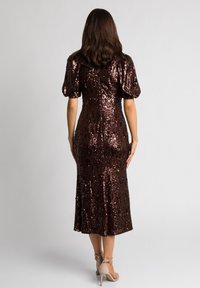 Brązowa sukienka z cekinami, z bufiastymi rękawami, dopasowanym fasonem, długością do kolan i gładką fakturą. Połączona z jasnymi szpilkami.