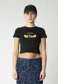 Klippt svart t-shirt med "drive"-tryck i gult och vitt, kombinerad med en högmidjad denimkjol med vågigt mönster och rå nederkant.