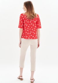 Röd blommig blus med kort ärm, matchad med ljusbeige cropped byxor och bruna sandaler med remmar. Strukturerad tyg, avslappnad passform.