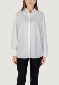 Camicia bianca con un motivo testurizzato, maniche lunghe e colletto. Abbinata a pantaloni neri per creare un contrasto.