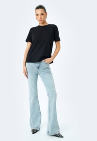 Sort bomulds t-shirt med korte ærmer, rund hals og præget tekst. Sammen med lyseblå flagrende jeans og sorte studsede hæle.