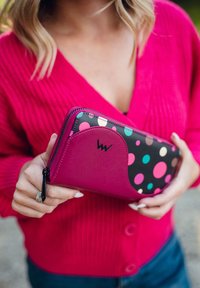 Pink wallet with a black polka dot design, featuring colorful dots. Smooth texture with a contrasting pocket, zipper closure, and logo detail.