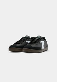 Black sneakers with a smooth texture, white side accents, and a brown outsole. Features round laces and a cushioned collar for comfort.