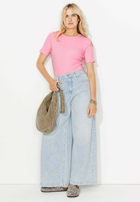 Haut rose à manches courtes ajusté, jeans taille haute bleu clair à jambes larges, sac à main gris décontracté et chaussures à imprimé animal sur fond blanc.