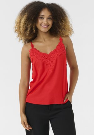 Rode camisole met kantdetails langs de halslijn. Voorzien van dunne bandjes en een losse pasvorm, gecombineerd met zwarte broeken.