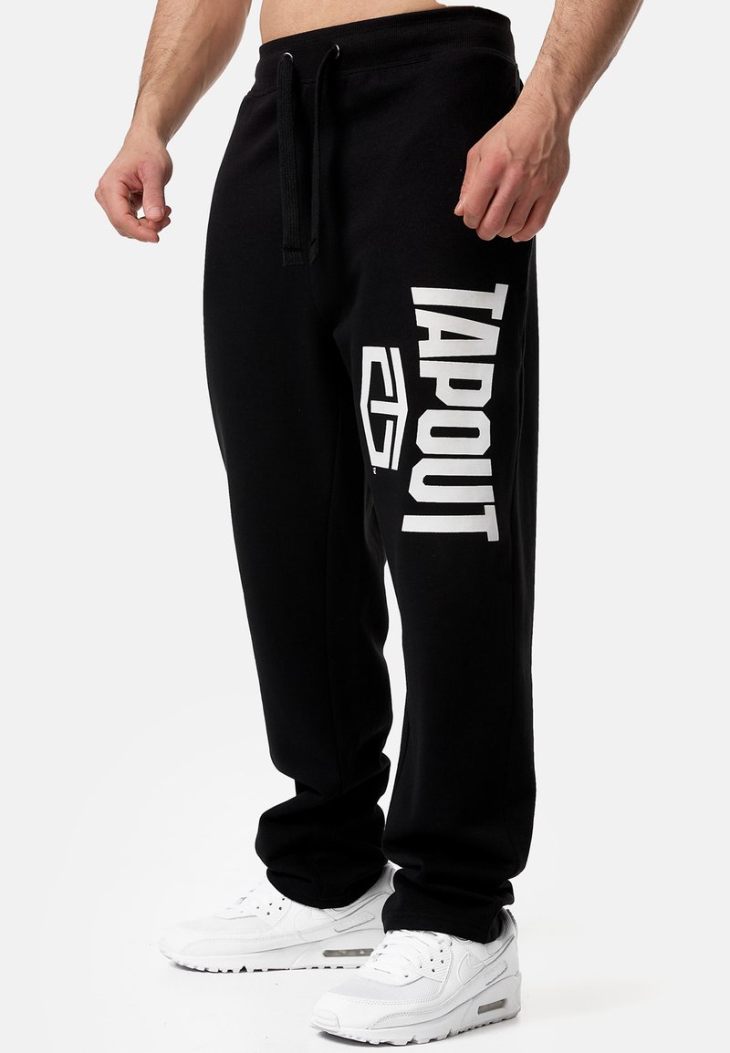 Fekete, puha anyagból készült melegítőnadrág széles derékkal, zsinórral, oldalzsebekkel és jól látható fehér „TAPOUT” logóval.