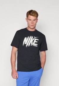 Camiseta de algodón negra con un gran logo blanco de Nike con diseño de pinceladas. Cuello redondo y mangas cortas. Corte simple y casual.