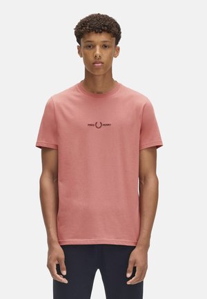 T-shirt a maniche corte, collo rotondo in cotone rosa chiaro. Caratterizzato da un logo nero "FRED PERRY" e una corona d'alloro al centro del petto.