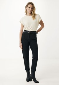 Top corto a maniche corte color crema con scollo ampio, abbinato a pantaloni neri a vita alta ben tagliati e stivali alla caviglia neri con tacco.