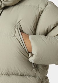 Giacca a vento imbottita in tessuto grigio chiaro con una texture trapuntata, caratterizzata da una mano in una tasca laterale e un cordoncino regolabile all'orlo.