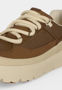 Baskets en cuir marron avec une semelle épaisse couleur crème et de larges lacets crème passés dans des œillets métalliques.