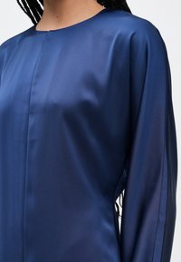 Tengerészkék szatén ruha kerek nyakkivágással, hosszú ujjakkal és sima, selymes textúrával. Minimalista dizájn oldalsó sliccel.