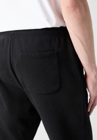Sorte bomulls joggebukser med elastisk midjebånd og en enkel baklomme. Glatt tekstur med et enkelt, funksjonelt design.