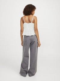 Hvit ermeløs peplum topp med detaljering av hull, sammen med vide grå jeans. Toppen har justerbare stropper og en samlet midje.