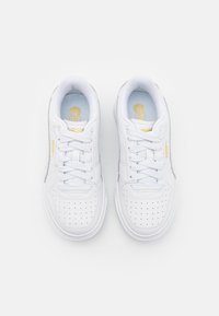 Baskets en cuir blanc avec motifs perforés, lacets plats, une semelle intérieure bleu clair et des accents dorés subtils sur la marque.