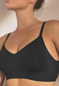 Black bra with a V-neck design, thin adjustable straps, and smooth texture. Features subtle horizontal lines on the sides.