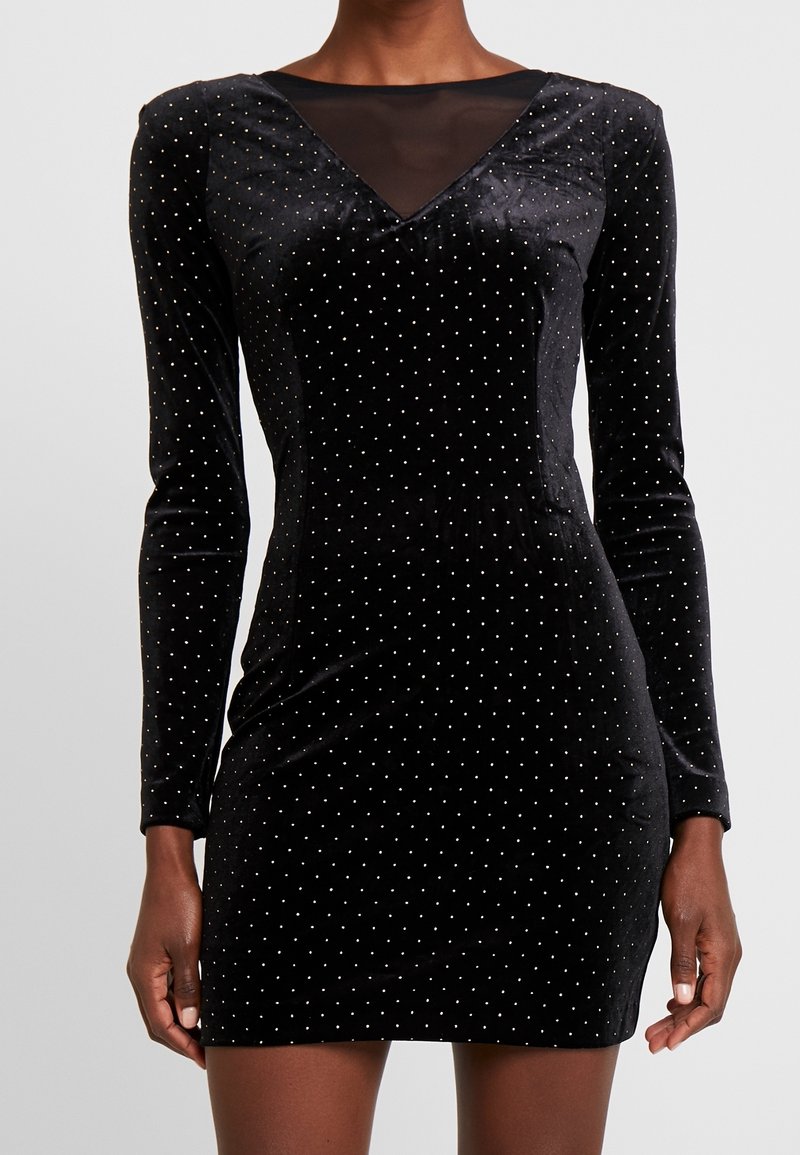 Schwarzes Samtkleid mit langen Ärmeln, V-Ausschnitt und transparenter Netz-Einlage. Verziert mit kleinen goldenen Punkten und hat eine körpernahe Silhouette.