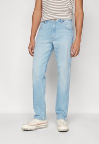 Lichtblauwe denim jeans met een rechte pasvorm, voorzien van een knoopsluiting, vijf zakken en subtiele vervagingen op de knieën. Draagt met witte sneakers.