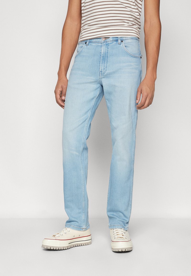 Lichtblauwe denim jeans met een rechte pasvorm, voorzien van een knoopsluiting, vijf zakken en subtiele vervagingen op de knieën. Draagt met witte sneakers.