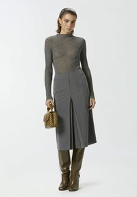 Siva prilagođena suknja s prednjim nabora, uparena s šik sivoj dugom rukavu majicom. Dodaci uključuju malu pufastu smeđu torbu i smeđe čizme.