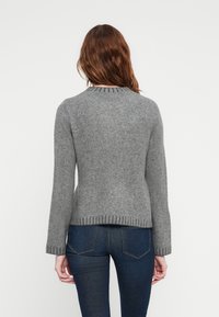 Grå strikket genser med lange ermer, ribbet hals og nederste kant. Mykt, strukturert stoff med en behagelig passform, båret over mørke jeans.