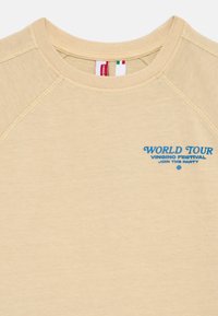 Béžová mikina s okrúhlym výstrihom vyrobená z mäkkej bavlny s raglánovými rukávmi. Obsahuje modrý grafický text: "Svetová tour Vingino festival Pridaj sa k párty."
