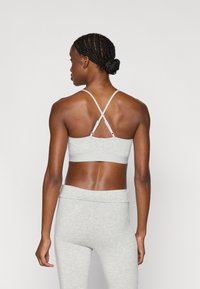 Γκρι αθλητικό σουτιέν με λεπτούς διασταυρωμένους ιμάντες στην πλάτη και απαλό ύφασμα. Φοράται με ταιριαστά γκρι κολάν, αποκαλύπτοντας έναν κομψό σχεδιασμό.