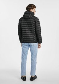 Czarna kurtka puchowa z poziomym przeszyciem i kapturem, noszona na jasnoniebieskich dżinsach i czarnych sneakersach. Gładka faktura i minimalistyczny design.