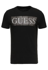 Zwarte katoenen T-shirt met een grafische print op de voorkant met het woord "GUESS" in het wit, omgeven door verticale streepdetaillering. Korte mouwen, ronde hals.