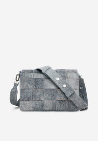 Szara torba na ramię z denimu o pikowanej strukturze, z metalowymi akcentami w kolorze srebrnym, regulowanym paskiem i kontrastowymi detalami stębnowania. Uformowany kształt.