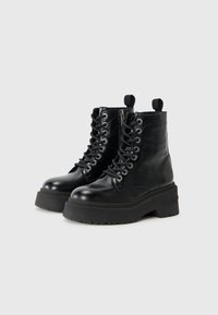 Bottines noires à semelle épaisse et à lacets, avec un côté marqué, sur fond blanc uni.