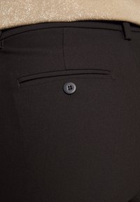 Zwarte broek met een gladde textuur, slim fit en een achterzak met een viergaatjes knoopaccent. De tailleband is op maat gemaakt.