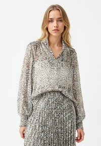 Transparante blouse met een V-hals en lange, opgeblazen mouwen, met een luipaardprint in beige en bruintinten, gecombineerd met een bijpassende rok.